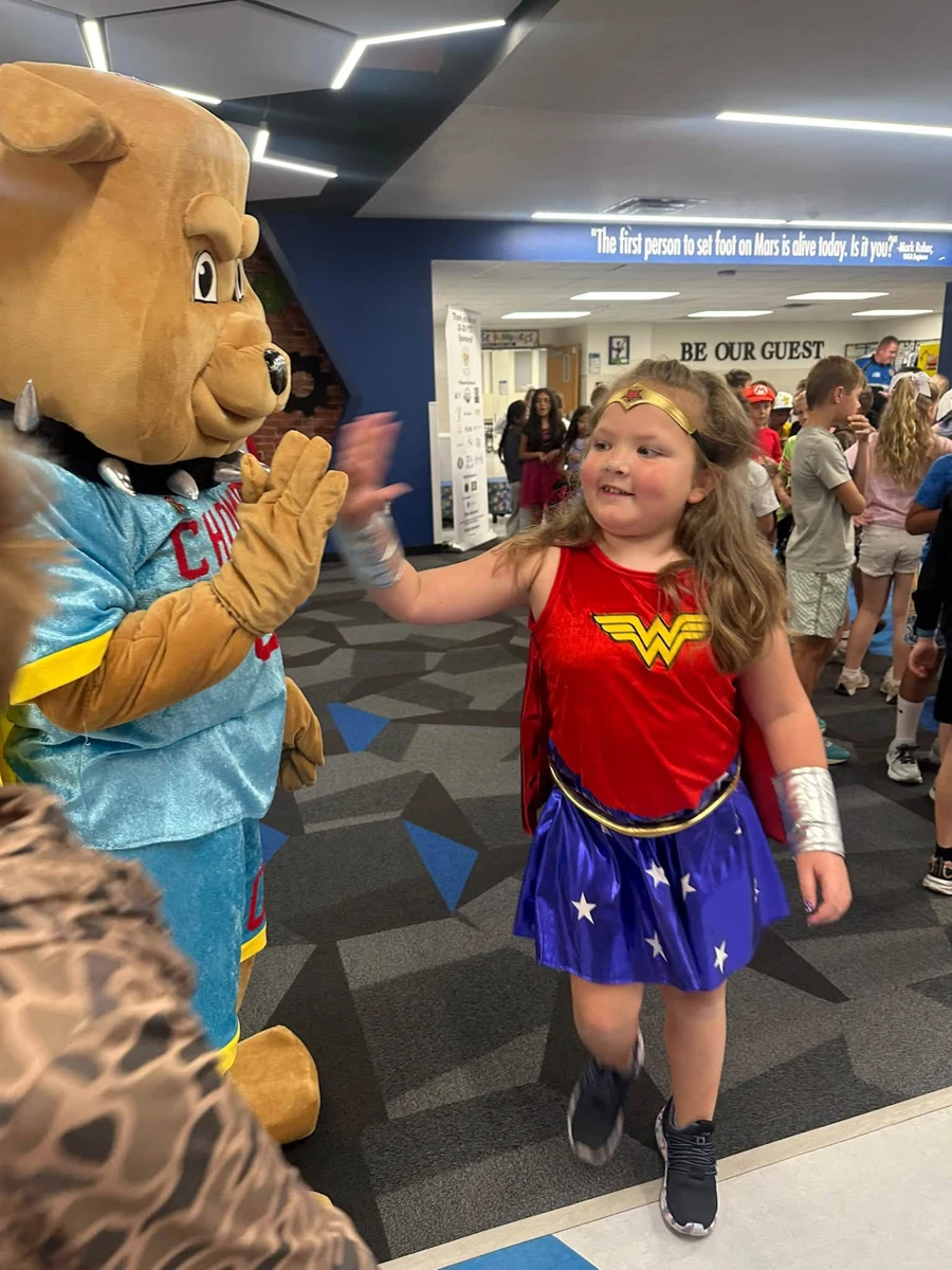 CHOMP mascot greeting a student in a superhero costume